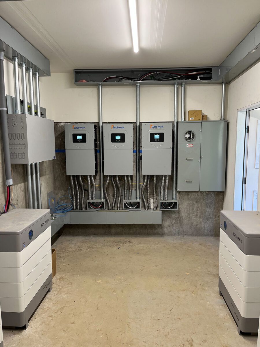 energy-storage10 A clean utility room in Santa Rosa with three large wall-mounted electrical control panels, a gray circuit breaker box, organized wiring, and two white solar battery energy storage units on the unfinished floor.