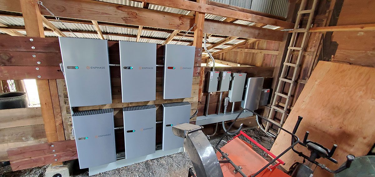 energy-storage14 Several silver Enphase battery storage units are mounted on a wooden wall inside a shed, part of a Santa Rosa solar battery energy storage setup surrounded by electrical conduit, tools, a ladder, and construction materials.