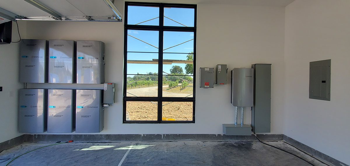 energy-storage5 A clean garage in Santa Rosa features wall-mounted solar battery energy storage units, electrical panels, and a large window letting in natural light. The unfinished floor and visible cables connect the advanced devices on the wall.